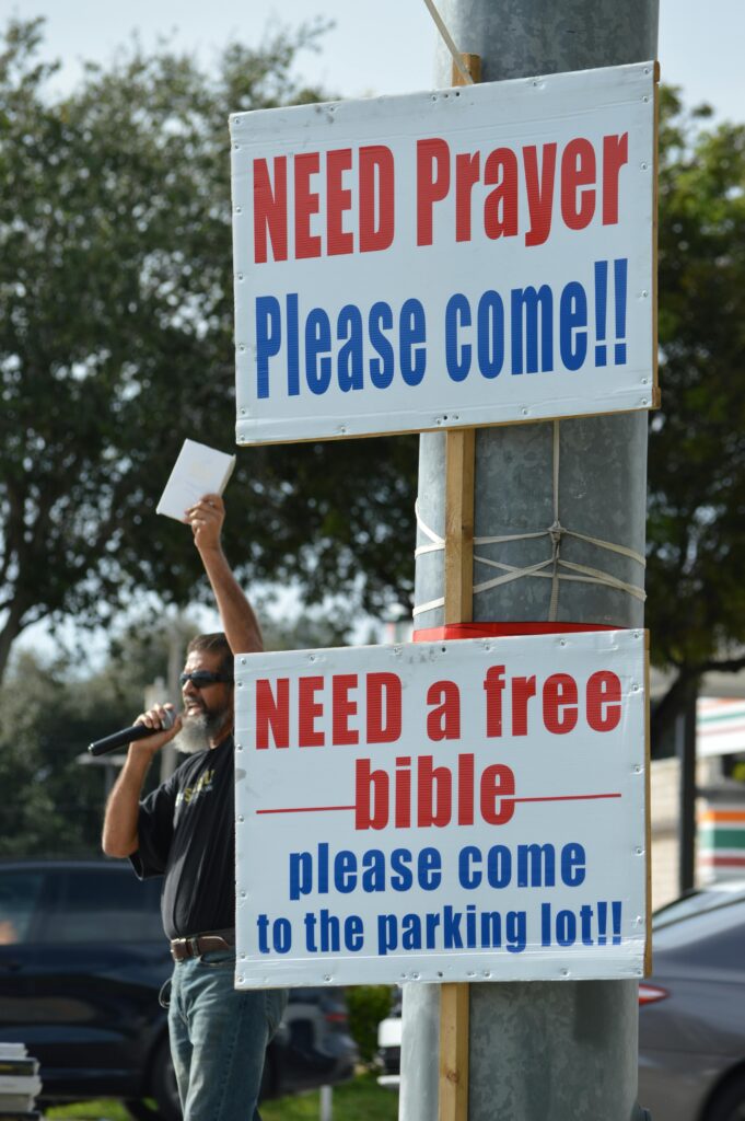 Outdoor signs invite prayer and free bibles with a speaker nearby.
