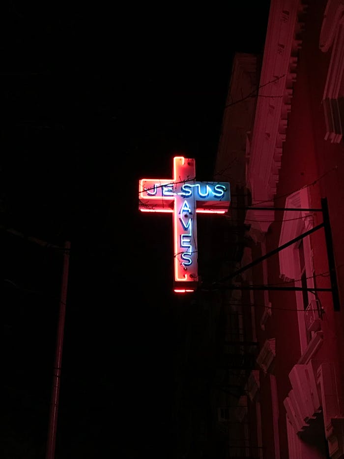 mobile-02 A glowing neon cross sign that reads 'Jesus Saves' against a dark night sky.
