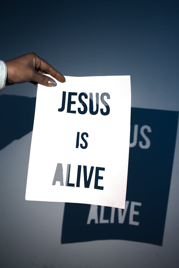 brand-02 A person holding a white paper with the message 'Jesus is Alive' against a blue background.