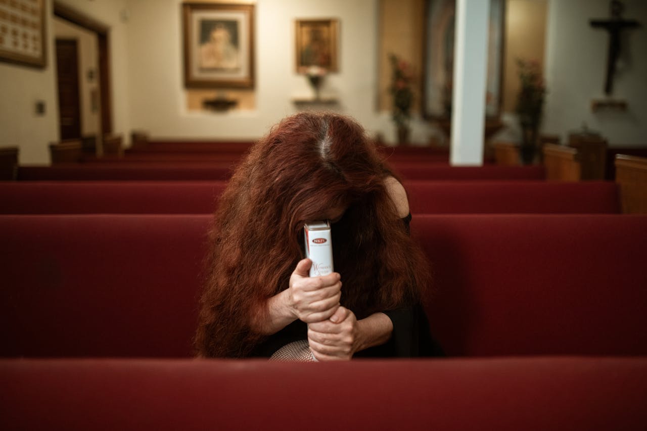 creative-02 A woman with red hair prays intensely in a church pew, holding a bible tightly.