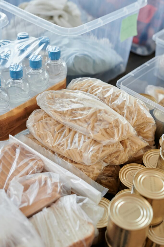 pexels photo 6994946 6994946 Packed groceries and canned food ready for donation. Includes pasta, water bottles, and bread.
