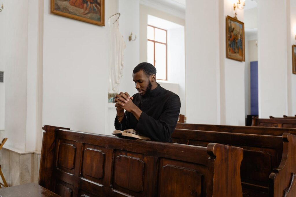 African American priest in deep prayer at a serene church setting.